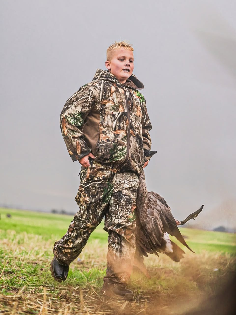 Young hunter carrying a Canada goose across a field