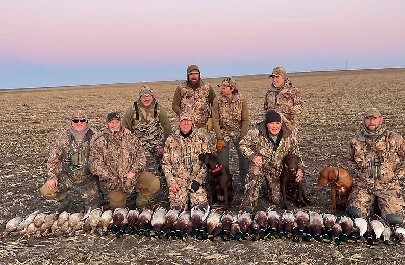 Group of hunters with a pile of ducks at dawn