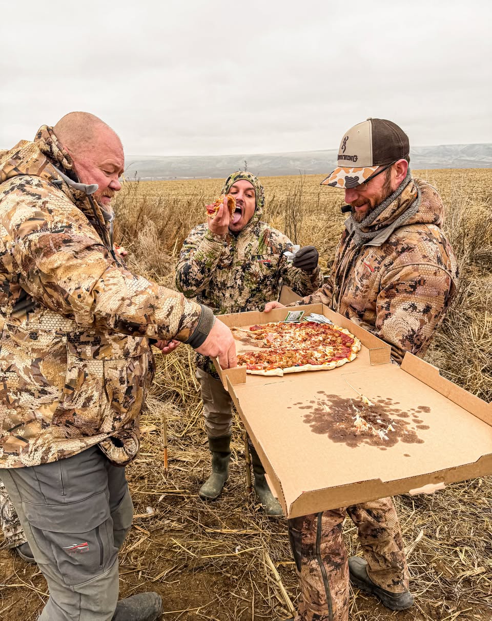 Three hunters sharing a pizza in the field blind