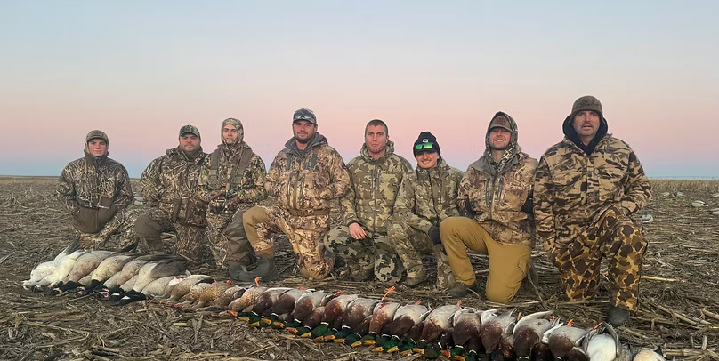 Eight hunters with a duck and goose pile at dusk
